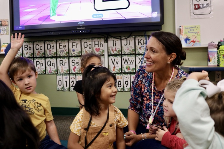 teacher surrounded by students on carpet