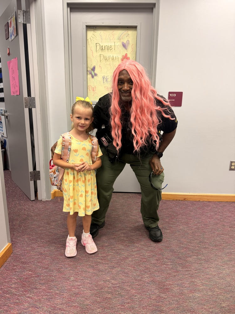 A person with pink hair and a costume poses with a young girl in a yellow dress.