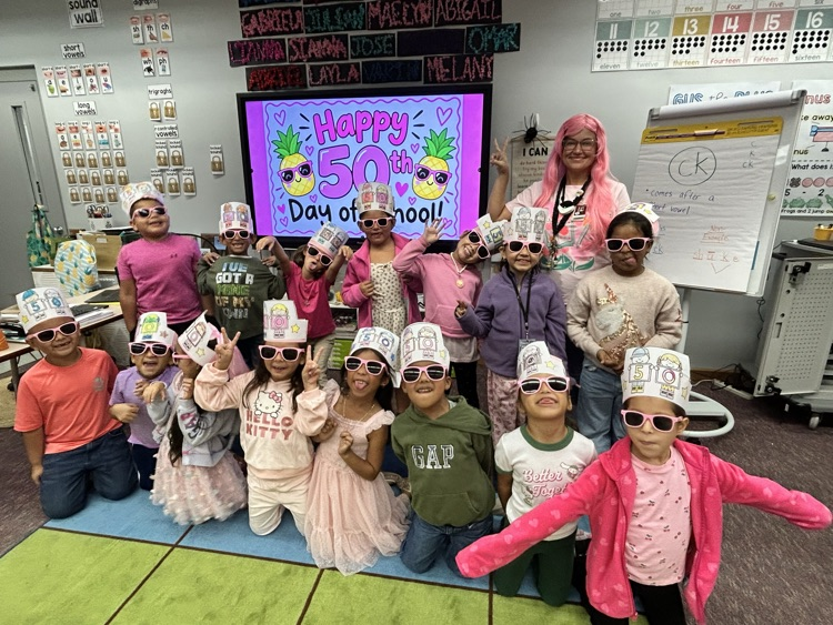 A group of students wearing hats and sunglasses poses for a photo in a classroom.