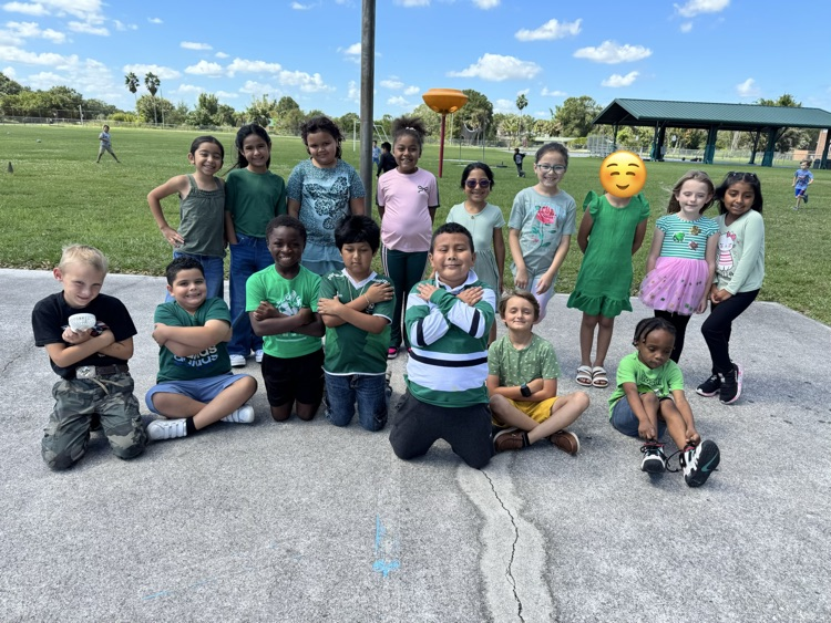 Group of young children wearing various colored shirts and shorts posing in a paved area outside.