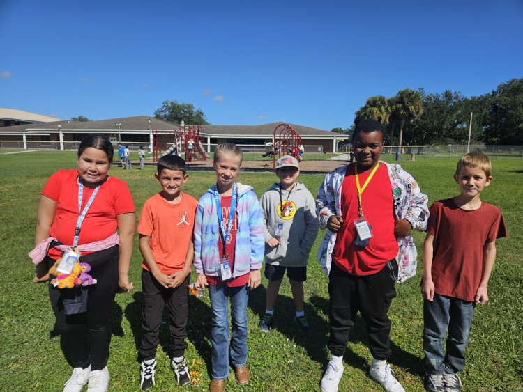Group of students with ID cards standing in a field with playground equipment in background.