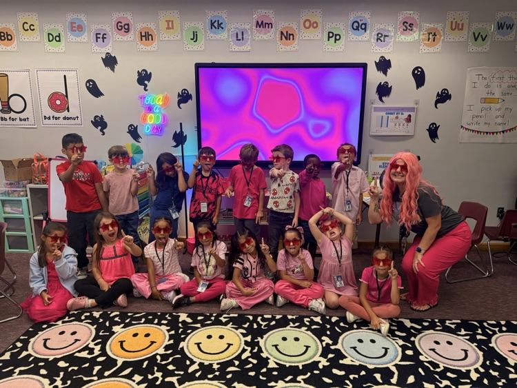 Group of students wearing glasses with heart lenses pose for a picture in front of a screen.