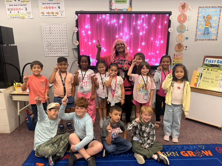 Group of children posing for a picture with a teacher, some standing, some sitting, in a classroom