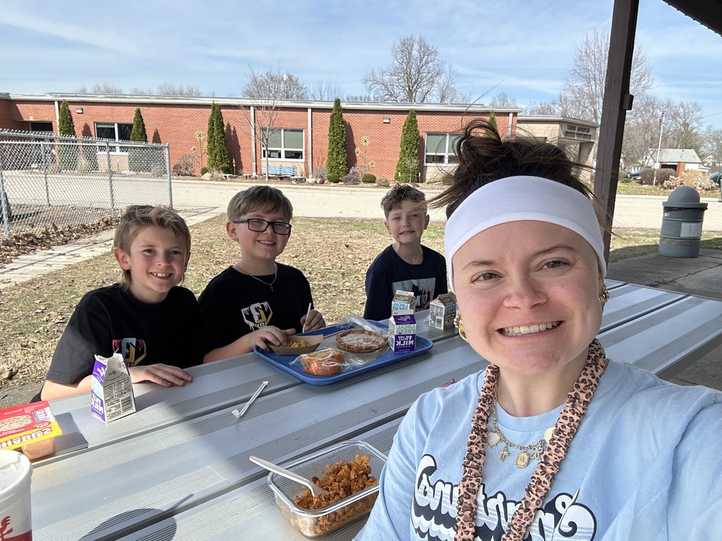 Three students eating at a picnic table with their teacher.