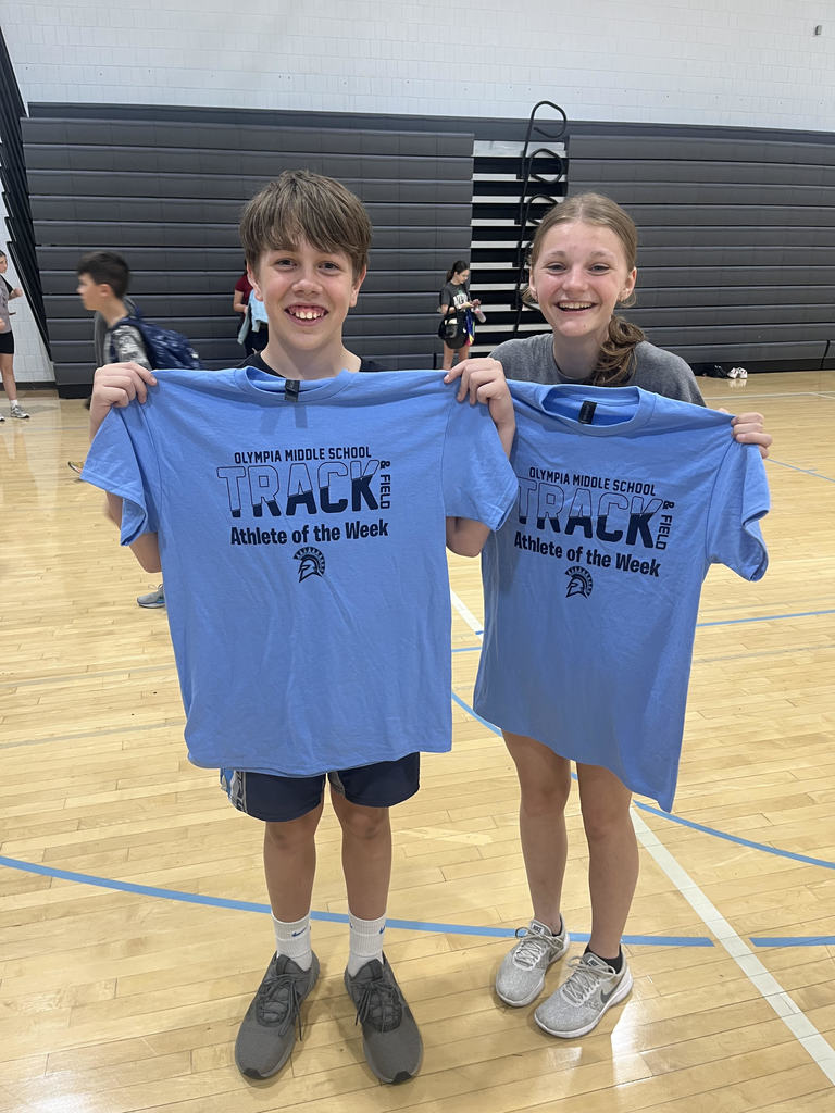 two track athletes standing next to each other holding up tshirts