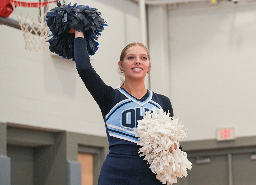 Cheerleader with blue and white pom poms leading a cheer
