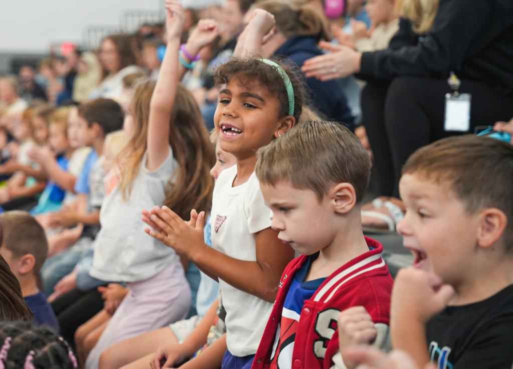 Students sitting in a school gym smiling and clapping hands