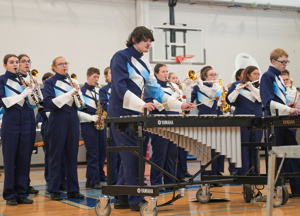 A school marching band in blue and white clothing perform in a gym
