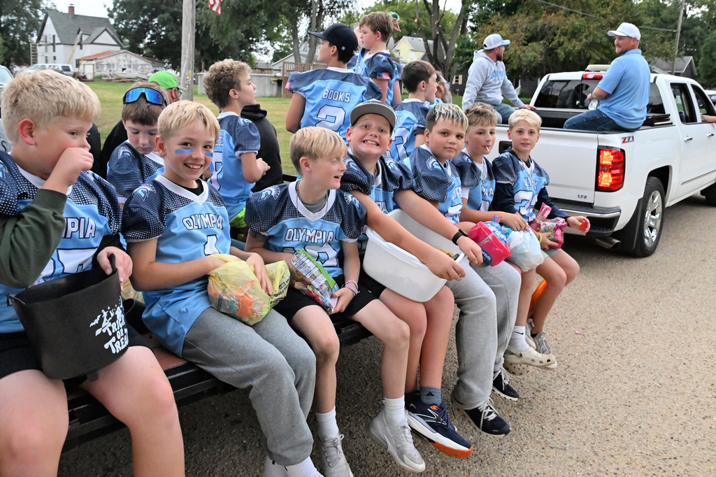 Students in light blue jerseys sit on the back of a flatbed truck in a parade
