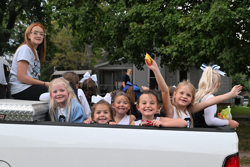 Female students sit on the back of a pickup truck in a parade route