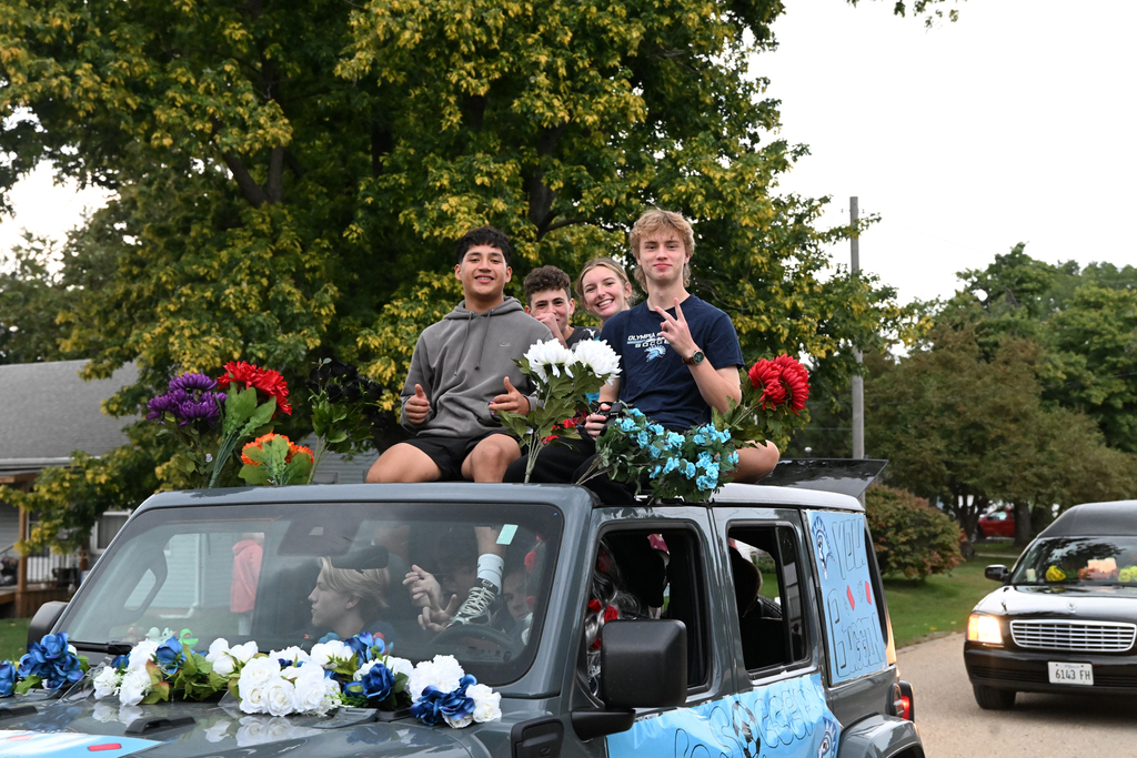 Four students sit on top of an open-roof jeep with flowers
