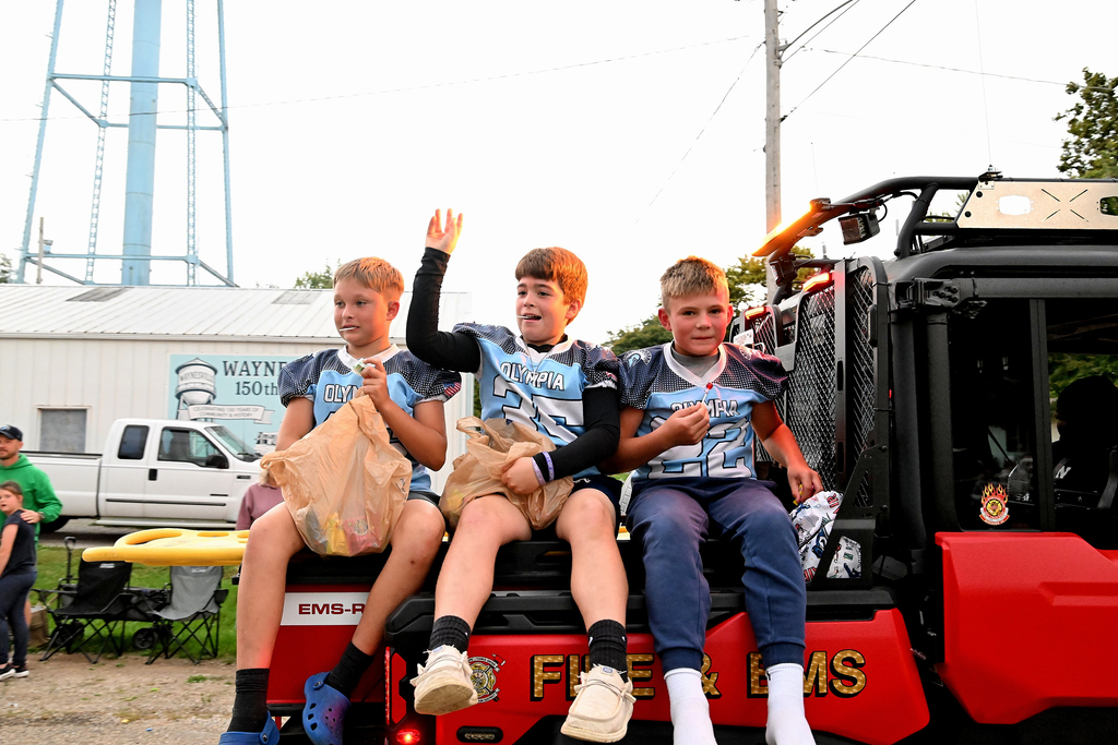Boys sit on the back of a flatbed truck waving and throwing candy