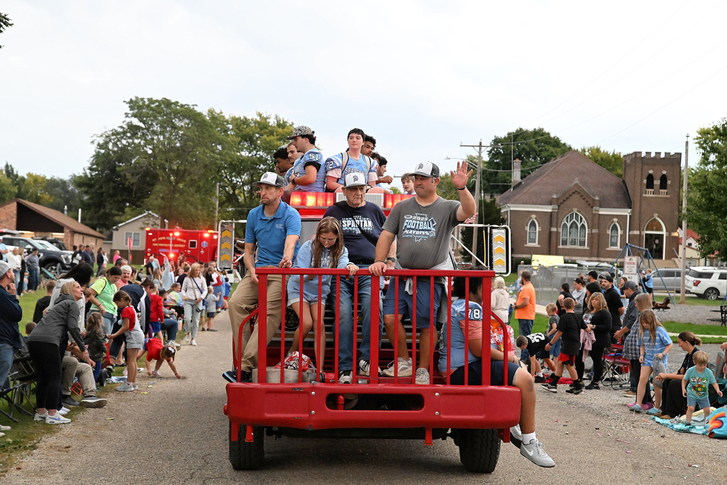 A group rides in the back of a pickup truck through a parade route