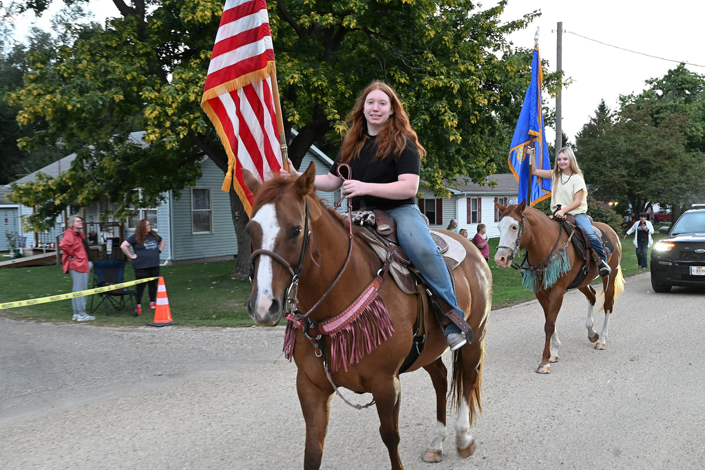 A girl in a black shirt sits on a brown horse holding an American falg