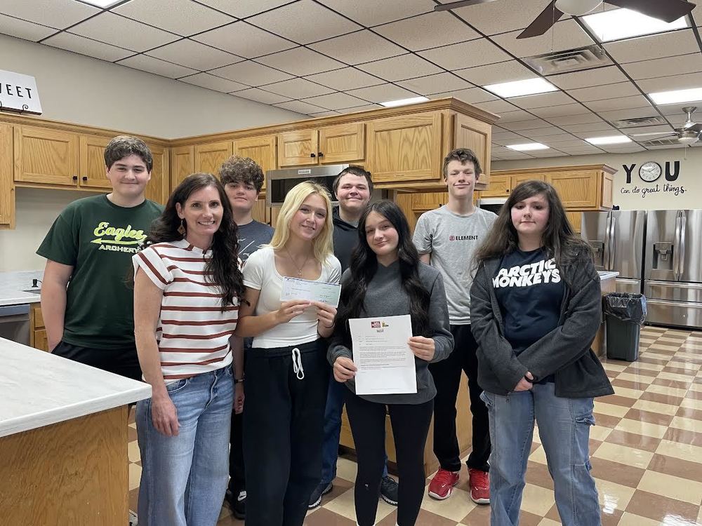 students and teacher standing in kitchen area holding a letter and a check for a grant received