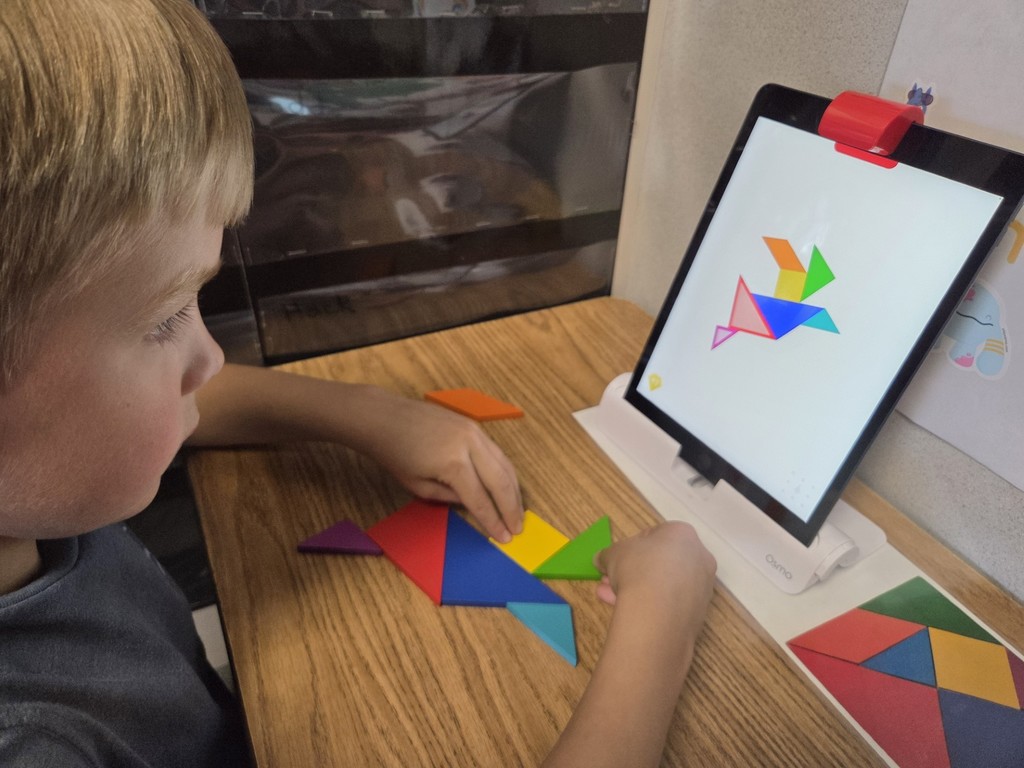 A kindergarten student is carefully placing shapes on the OSMO tangrams game.
