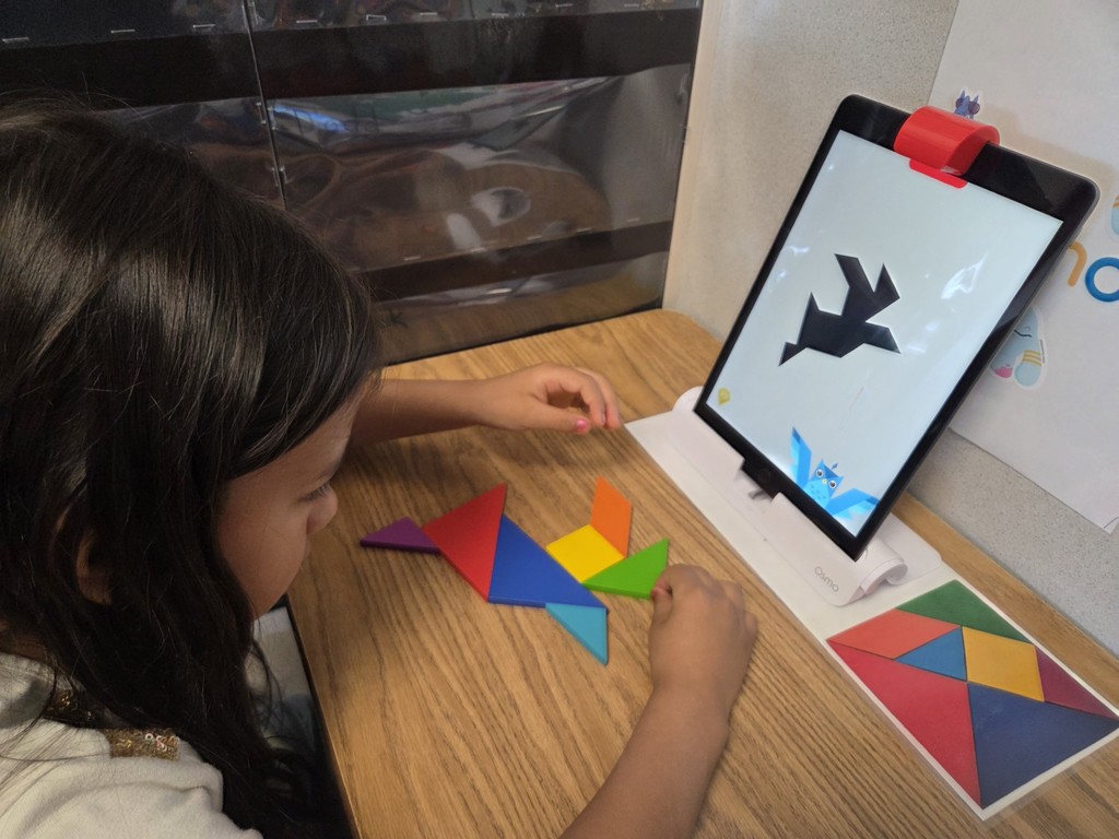 A student has almost solved a puzzle using colored shapes on OSMO tangrams.