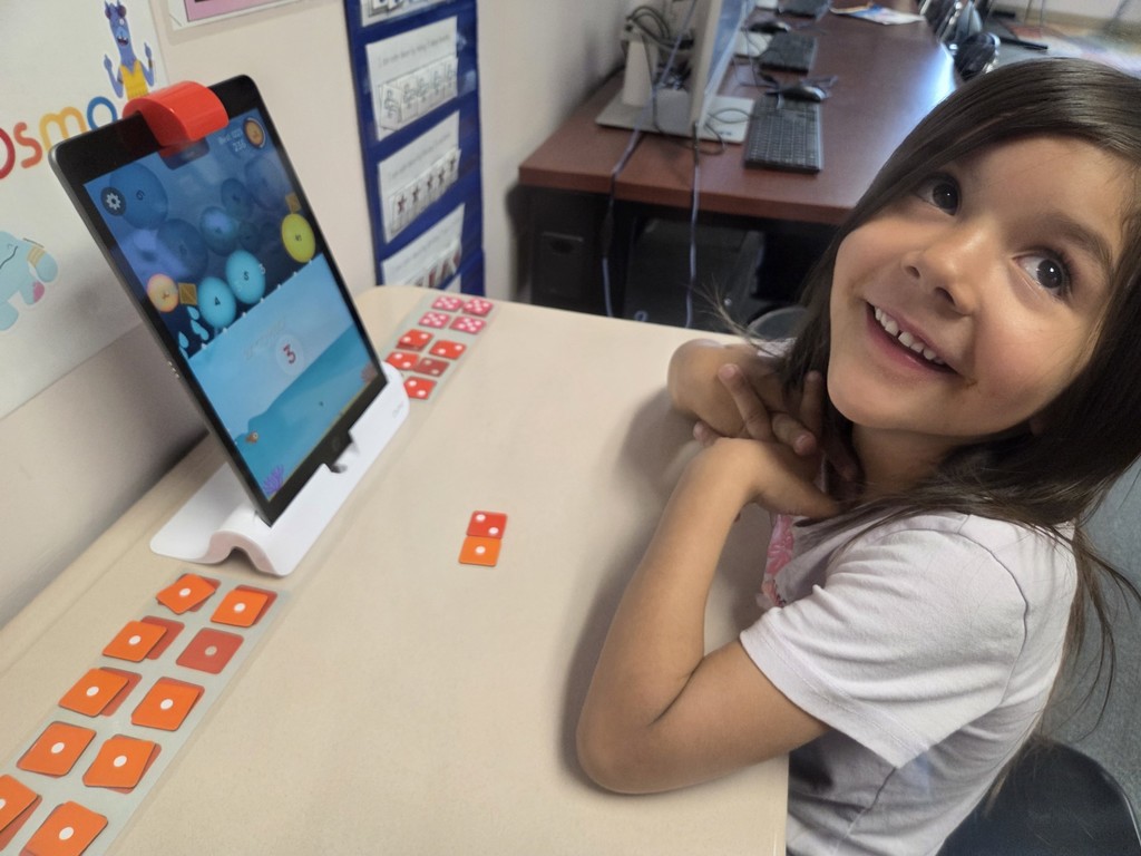 A kindergarten student uses OSMO number tiles to pop bubbles to fill a virtual fishtank.