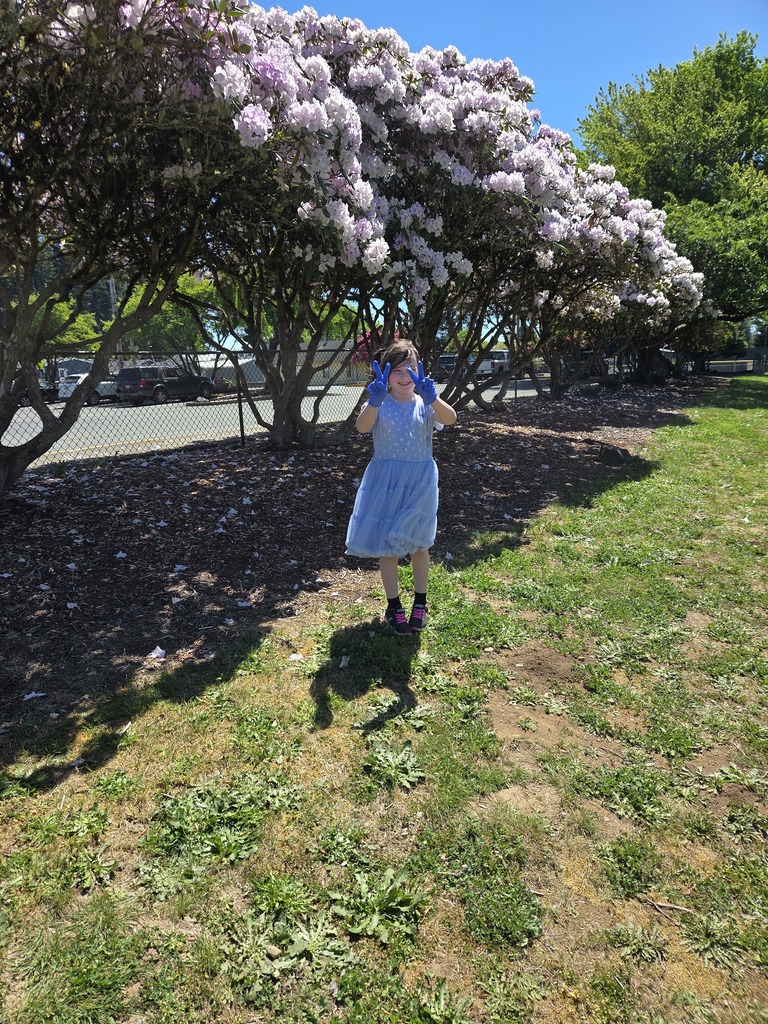 student giving peace sign standing by bushes