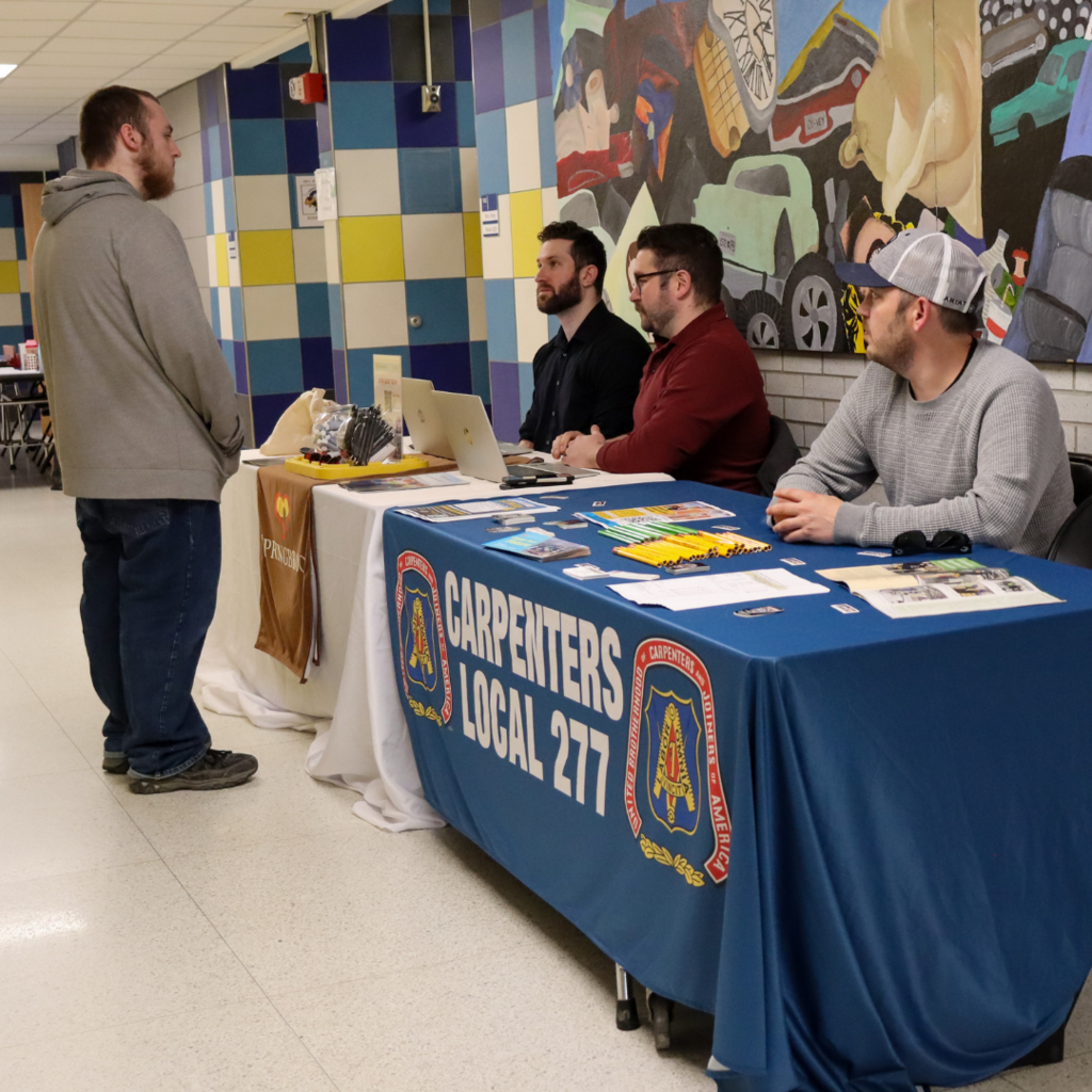 student speaking with 3 men behind a table.