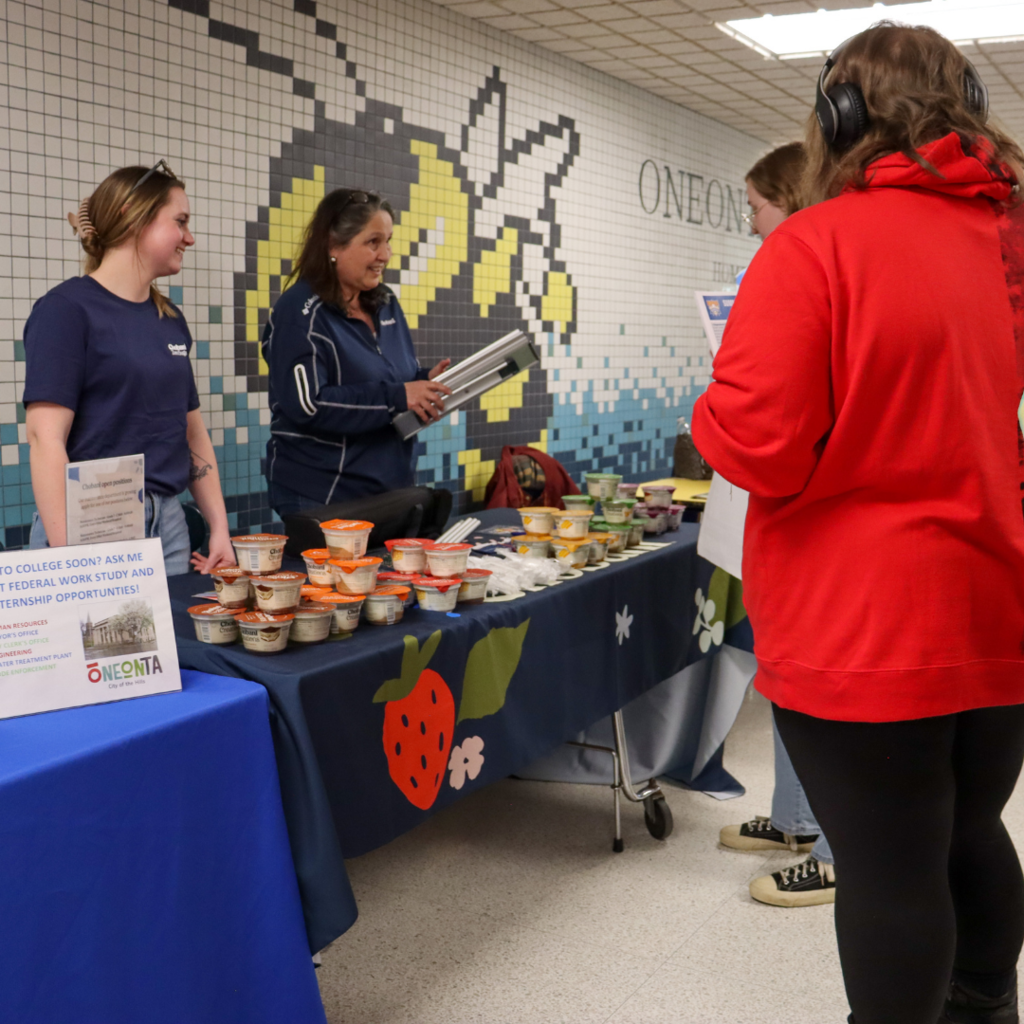 students talking to two women behind a table of yogurt.