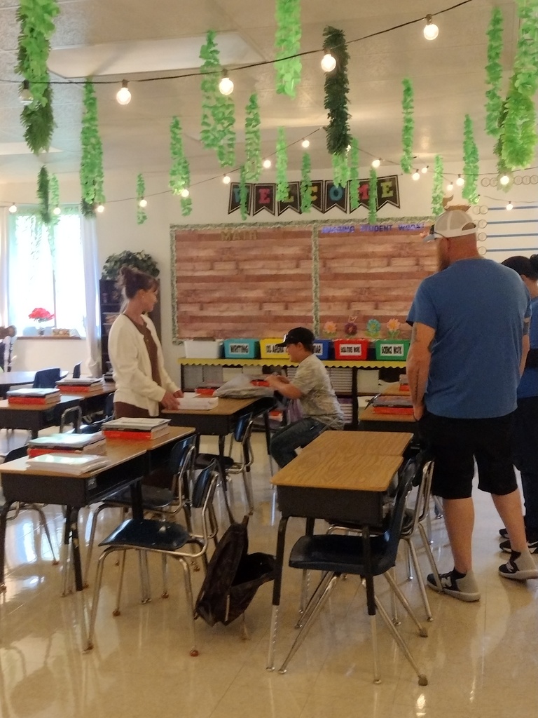 Adults and a student gather in a decorated classroom with hanging greenery, string lights, and prepared desks.