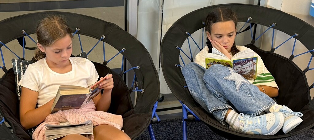 Two students sitting in chairs reading books