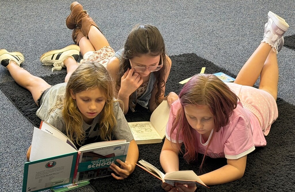 Three students laying down reading books in a library