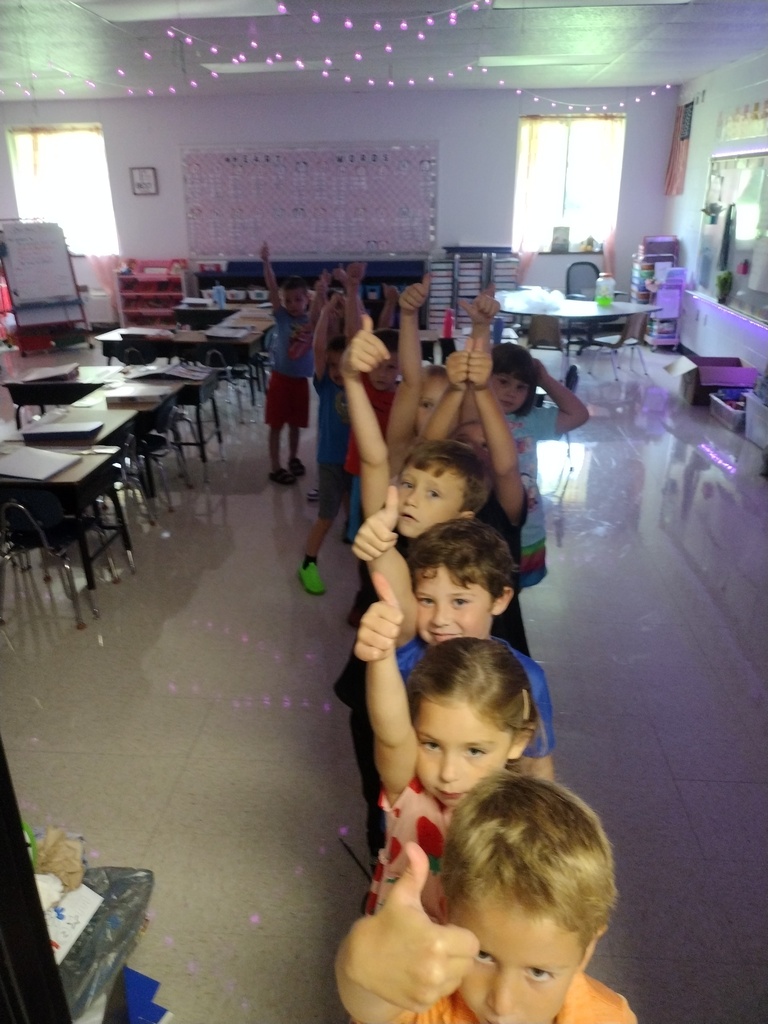 Children lined up in a classroom giving the thumbs up sign.