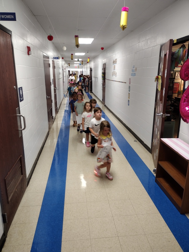 Children in a line walking down a school hallway with blue stripes on the floor