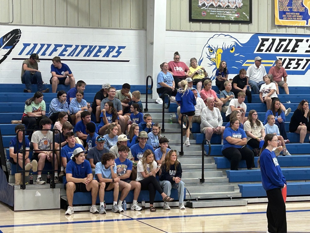 Spectators in blue bleachers watch a school sporting event beneath Trailfeathers and Eagles West wall graphics.