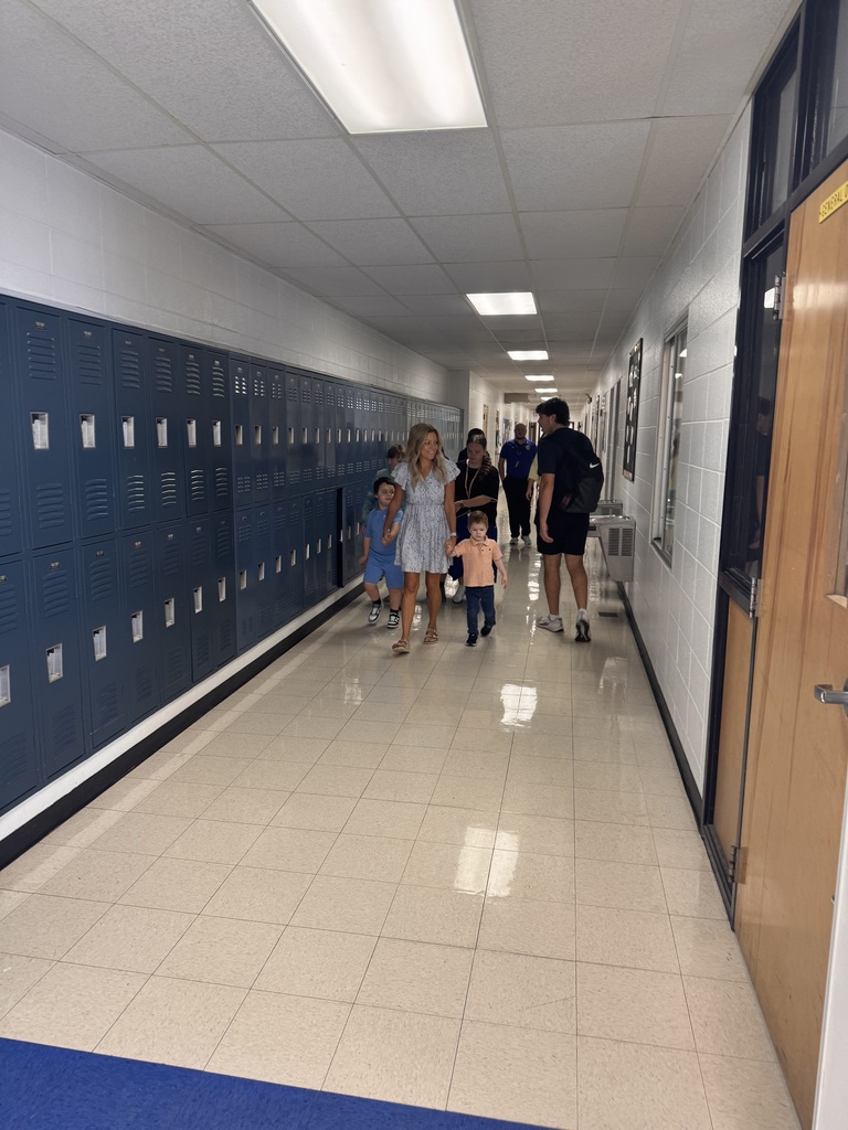 Teacher leading several students down a hallway with blue lockers on the wall.
