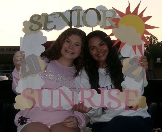 Two students smile while holding a handmade “Senior Sunrise 2027” frame decorated with clouds and a sun.