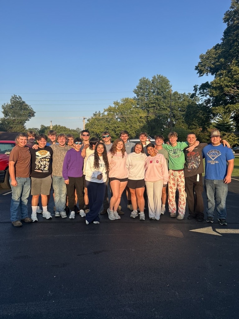 A large group of students poses together in a school parking lot during a sunny senior sunrise gathering.