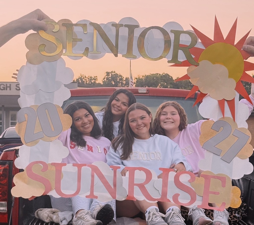 Four students pose inside a handmade “Senior Sunrise 2027” frame at sunset, seated in the back of a vehicle.