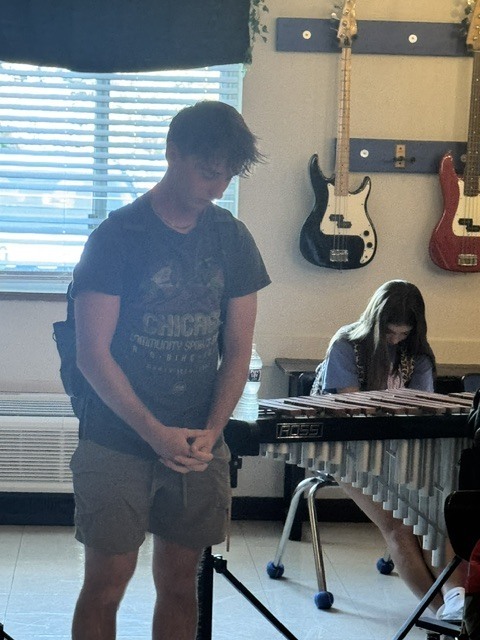 Student stands with head bowed and hands clasped while another student sits behind a vibraphone.