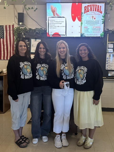 Four women smile together wearing matching “Make Disciples of All Nations” shirts at an FCA gathering.