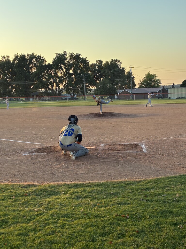 Image 3: Pitcher delivers the ball toward a crouching catcher during a baseball game at sunset.