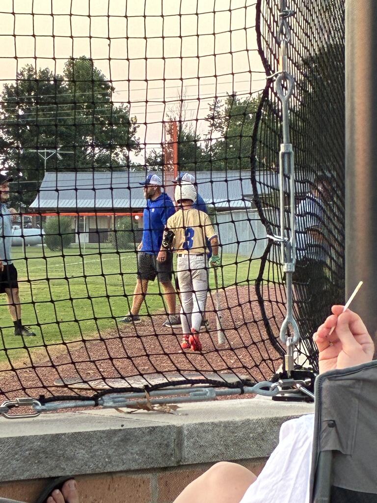 Image 2: Baseball player wearing number 3 walks near the dugout with coaches during an evening game.