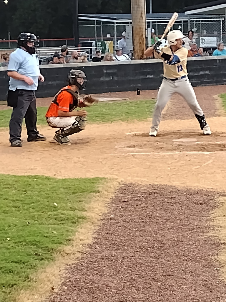Baseball batter in a cream uniform prepares to swing as the catcher crouches and the umpire watches behind him.