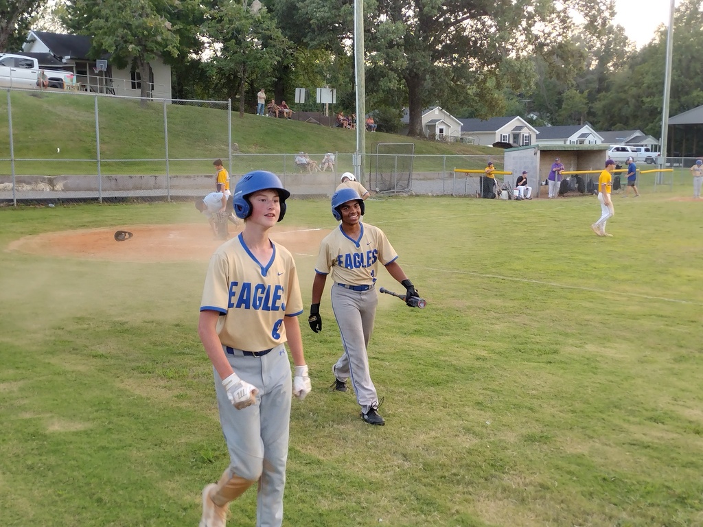 Two smiling Eagles baseball players in helmets walk off the field together, one carrying a bat.