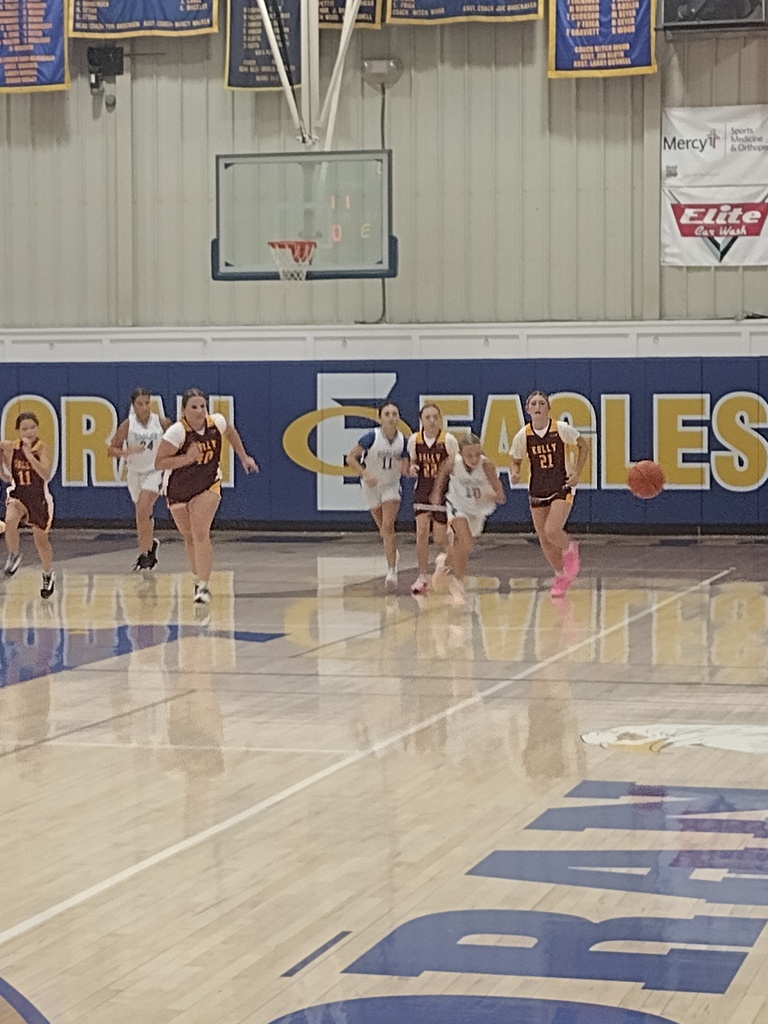 Girls’ basketball players in white and maroon uniforms sprint down the court toward a loose ball.