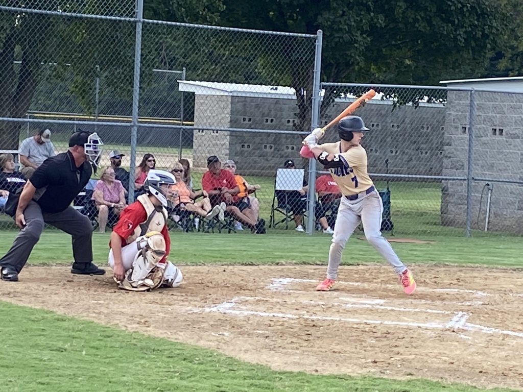 Baseball player in a tan jersey with a number 7 holding his bat waiting to swing at the pitch.