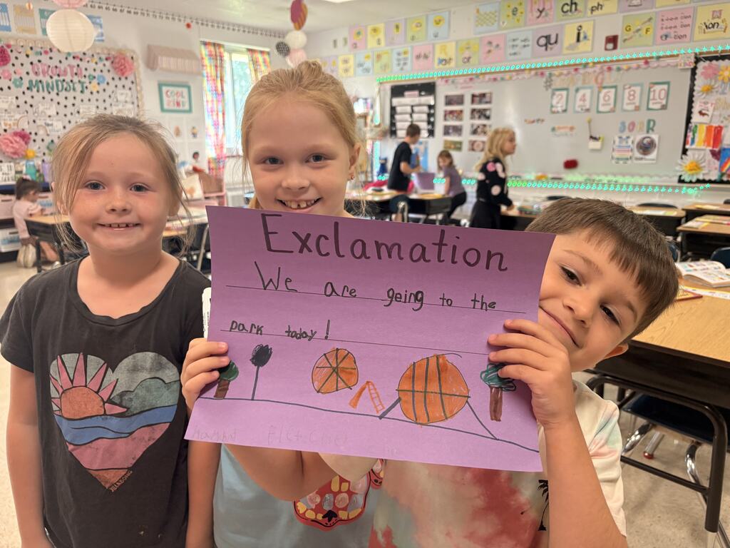 Three students hold a purple “Exclamation” poster reading, “We are going to the park today!” with colorful drawings.