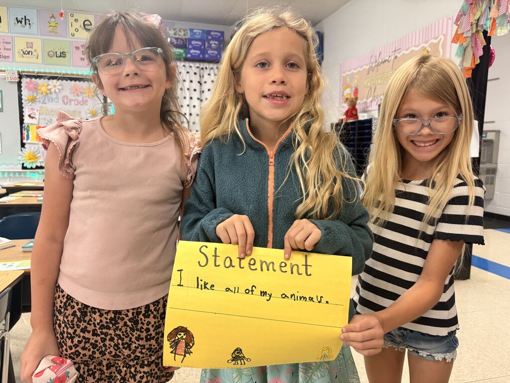 Three students pose with a yellow “Statement” poster reading, “I like all of my animals,” with drawings underneath.