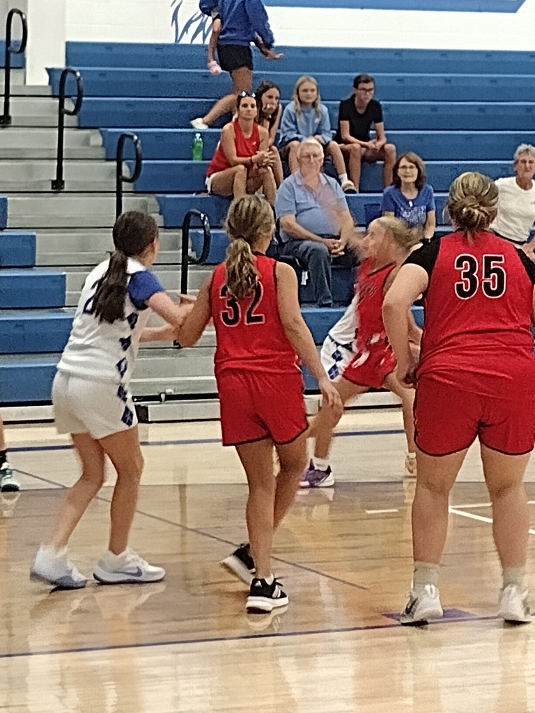 Young girls basketball players in white jerseys and red jerseys playing in a gymnasium.