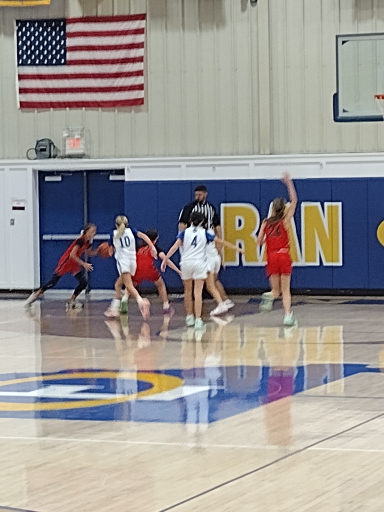 Young girls basketball players in white jerseys and red jerseys playing in a gymnasium.