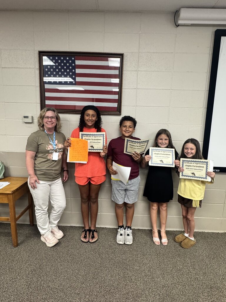 Four young students standing next to a teacher against a wall holding certificates and smiling
