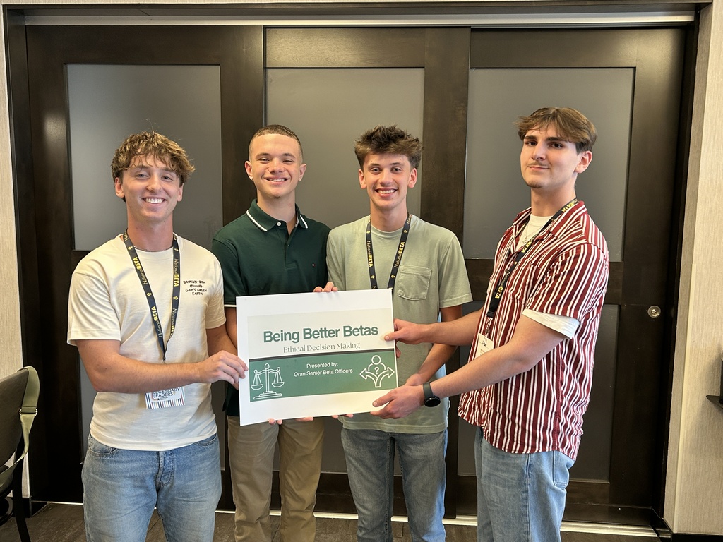 Four students pose indoors holding a “Being Better Betas: Ethical Decision Making” presentation sign.