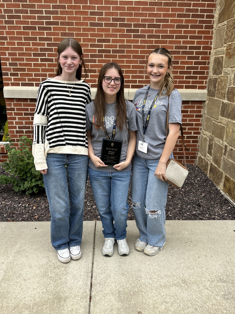 Three students pose outside a brick building; the center student holds a Beta Blitz outstanding qualifier plaque.